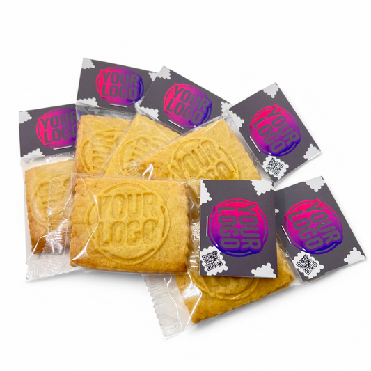 Mehrere einzeln verpackte Logokekse mit Logo und QR-Code auf dem Label, lose arrangiert auf weißem Hintergrund – perfekt als Streuartikel oder visuelle Visitenkarte für Unternehmen