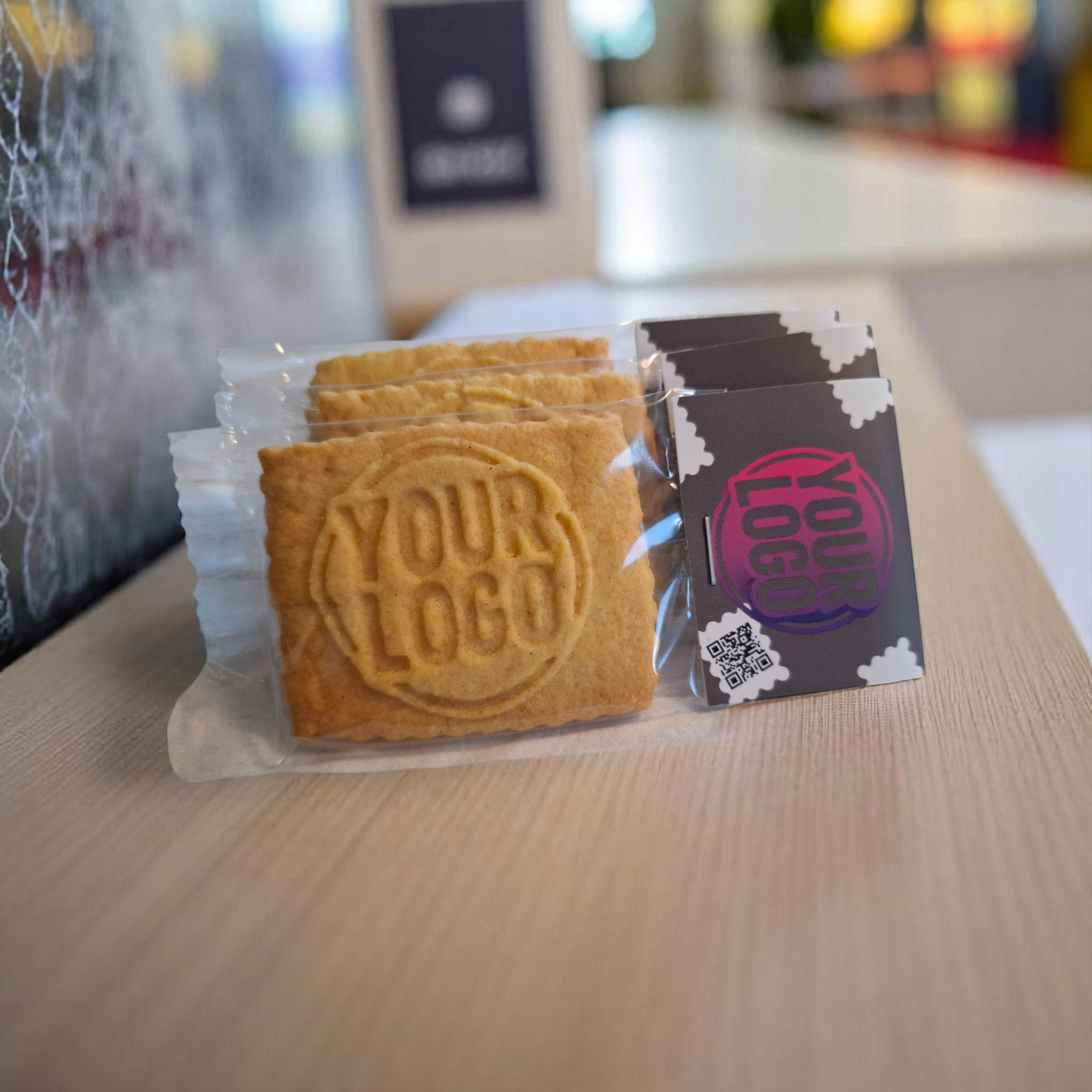 Drei einzeln verpackte Logokekse mit Logo-Prägung und auffälligem Keksreiter auf einer Theke – ideal als Visitenkartenersatz, Kundengeschenk oder für die Hotellerie